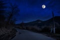 Mountain Road through the forest on a full moon night. Scenic night landscape of country road at night with large moon. Long Royalty Free Stock Photo