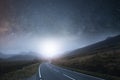 A mountain road heading into the distance at night with stars in the sky with a bright light glowing on the horizon Royalty Free Stock Photo