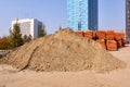 A mountain of sand and many pallets of bricks. A construction site against a backdrop of residential buildings.