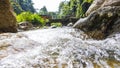 A mountain stream flows rapidly between the rocks on a narrow bridge in the rainforest of the Cameron Highlands, Malaysia. The Royalty Free Stock Photo