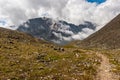 A mountain trail leads to a high mountain surrounded by clouds.