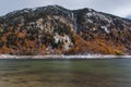 A mountain with trees and a snowy in front of a lake