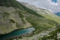 A mountain valley landscape with green hills, turquoise lake and white clouds. Two little blue tents among wild nature Royalty Free Stock Photo