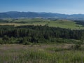 Mountain valley with meadow, forest, green fileds and with blue misty slopes of low tatra mountais in the distance