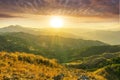 Mountain valley during sunset or sunrise. Rocks and slopes covered with green trees with amazing cloudy sunny sky on background Royalty Free Stock Photo