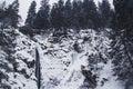 Mountain waterfall with rocks and cliffs covered with snow during snowfall, the mountains trees Royalty Free Stock Photo