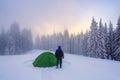 Mountain winter landscape. Tourist stands on the path next to the green tent. Wild forest. Pine tree. A lawn covered with snow. Royalty Free Stock Photo