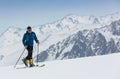 Mountaineer backcountry ski walking up along a snowy ridge with skis in the backpack. In background blue sky and shiny