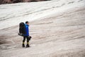 A mountaineer with a backpack walks in wheelchairs, stands on a dusty glacier with sneakers in the hands between cracks Royalty Free Stock Photo