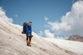 A mountaineer with a backpack walks in wheelchairs, stands on a dusty glacier with sneakers in the hands between cracks Royalty Free Stock Photo