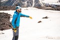 A mountaineer in a cap with glasses and an ice pick stands on a background of a snow-capped mountain Royalty Free Stock Photo