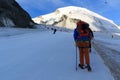 Mountaineer with crampons ascending towards mountain Allalinhorn on ski slope, skiers and snow mountain panorama in Saas-Fee,