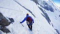 Mountaineer with ice ax reaches the top of a snowy mountain in a sunny winter day