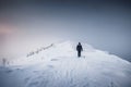 Mountaineer man walking on snowy mountain ridge with blizzard in gloomy weather at Senja island Royalty Free Stock Photo