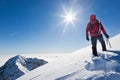 Mountaineer reaches the top of a snowy mountain in a sunny winter day.