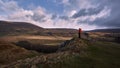 Mountaineer in red jacket on a hill on the isle of skye, scotland looking towards a waterfall in a mountainous landscape. cloudy