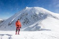 Mountaineer standing in a snowed landscape with a high peak behind him.