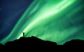 Mountaineer standing on top of mountain with Aurora Borealis glowing in the night sky on arctic circle