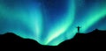 Mountaineer standing on top of mountain with Aurora Borealis glowing in the night sky on arctic circle