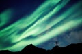 Mountaineer standing on top of mountain with Aurora Borealis glowing in the night sky on arctic circle