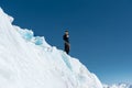 A mountaineer stands on the edge of a glacier with a snow shovel in his hands and shows Shak`s gesture against the blue