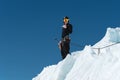 A mountaineer stands on the edge of a glacier with a snow shovel in his hands and shows Shak`s gesture against the blue