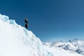 The mountaineer stands on the edge of the glacier with a snow shovel in his hands and shows Shak`s gesture against the