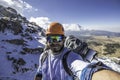 Mountaineer taking a selfie with a camping backpack and a landscape full of snow and rocks with an active volcano in the