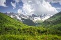 Mountains landscape. Rocky mountains with snowy peaks, green hills covered by grass in Alpine scene on bright sunny day Royalty Free Stock Photo