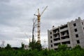 Mounting crane at construction of apartment building, green trees in the foreground, horizontal composition, cloudy rainy sky Royalty Free Stock Photo
