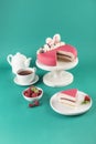 Mousse cake with a cut piece with raspberries on a wooden white stand with a teapot and a cup of tea on a bright green background Royalty Free Stock Photo