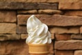 Mouthwatering Vanilla Soft Serve Ice Cream Cone Against Blurry Brown Stone Blocks Wall
