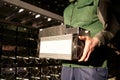 Mover holding bitcoin ASIC miner in warehouse. Worker with ASIC mining equipment on stand racks for mining