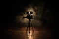 Movie concept. Miniature movie set on dark toned background with fog and empty space. Silhouette of vintage camera on tripod