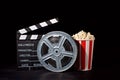 Movie film reel and film clapper with popcorn box on black Royalty Free Stock Photo