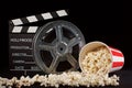 Movie film reel and film clapper with popcorn box on black Royalty Free Stock Photo