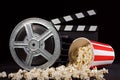 Movie film reel and film clapper with popcorn box on black Royalty Free Stock Photo