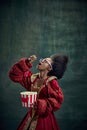 Movie night. African young girl, medieval princess eating popcorn against vintage green background. Historical portrayal