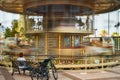 The moving carousel and the woman sitting on the bench next to a bicycle