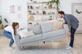 Moving or permutation furniture at home. Happy guy and girl raise sofa in interior of living room Royalty Free Stock Photo