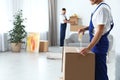 Moving service employee sealing cardboard box with adhesive tape in room