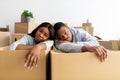 Moving stress concept. Exhausted black family leaning on unpacked boxes, having problems during relocation