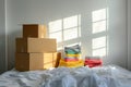 Moving to new home. Stack of cardboard boxes with household belongings, pile of clothes on messy bed in empty room. Real Royalty Free Stock Photo