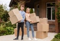 Moving to new house. Young guy with his wife holding cardboard boxes in front of their home Royalty Free Stock Photo