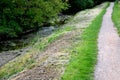 Mowing the grass along the water flow of the stream by the path of gravel gray dry cut grass on the slope above the stream