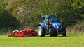 Mowing the grass in the park. Blue tractor red cutting machine