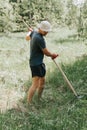 mowing the grass traditional old-fashioned way with the hand scythe on the household village farm. young mature farmer Royalty Free Stock Photo