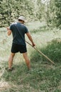 mowing the grass traditional old-fashioned way with the hand scythe on the household village farm. young mature farmer Royalty Free Stock Photo