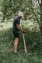 mowing the grass traditional old-fashioned way with the hand scythe on the household village farm. young mature farmer Royalty Free Stock Photo