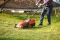 Mowing trimmer - worker cutting grass in green yard at sunset. Man with electric lawnmower, lawn mowing. Gardener Royalty Free Stock Photo